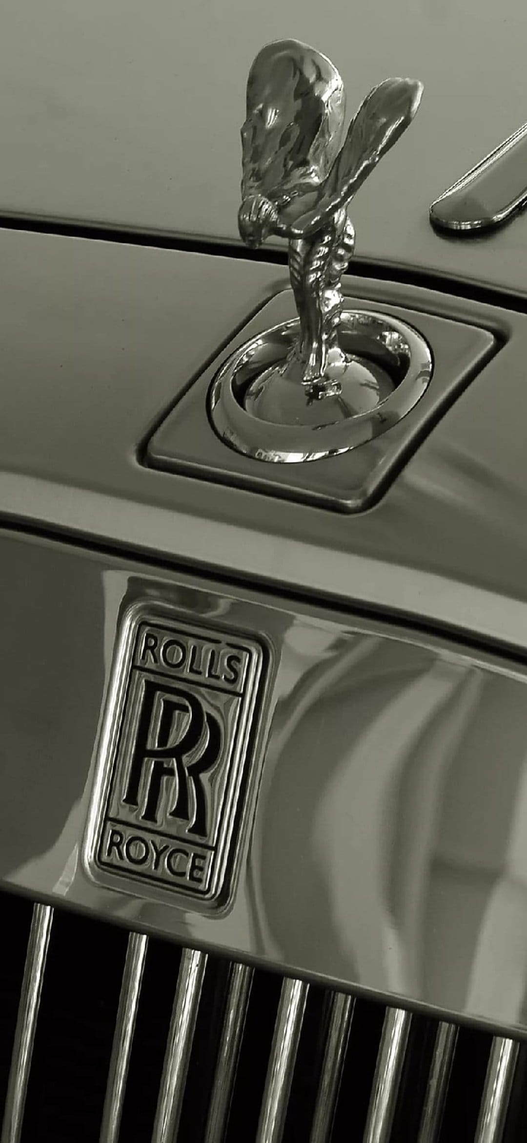 Spirit of Ecstasy figurine stands on a polished chrome grille with the Rolls-Royce emblem in monochrome.