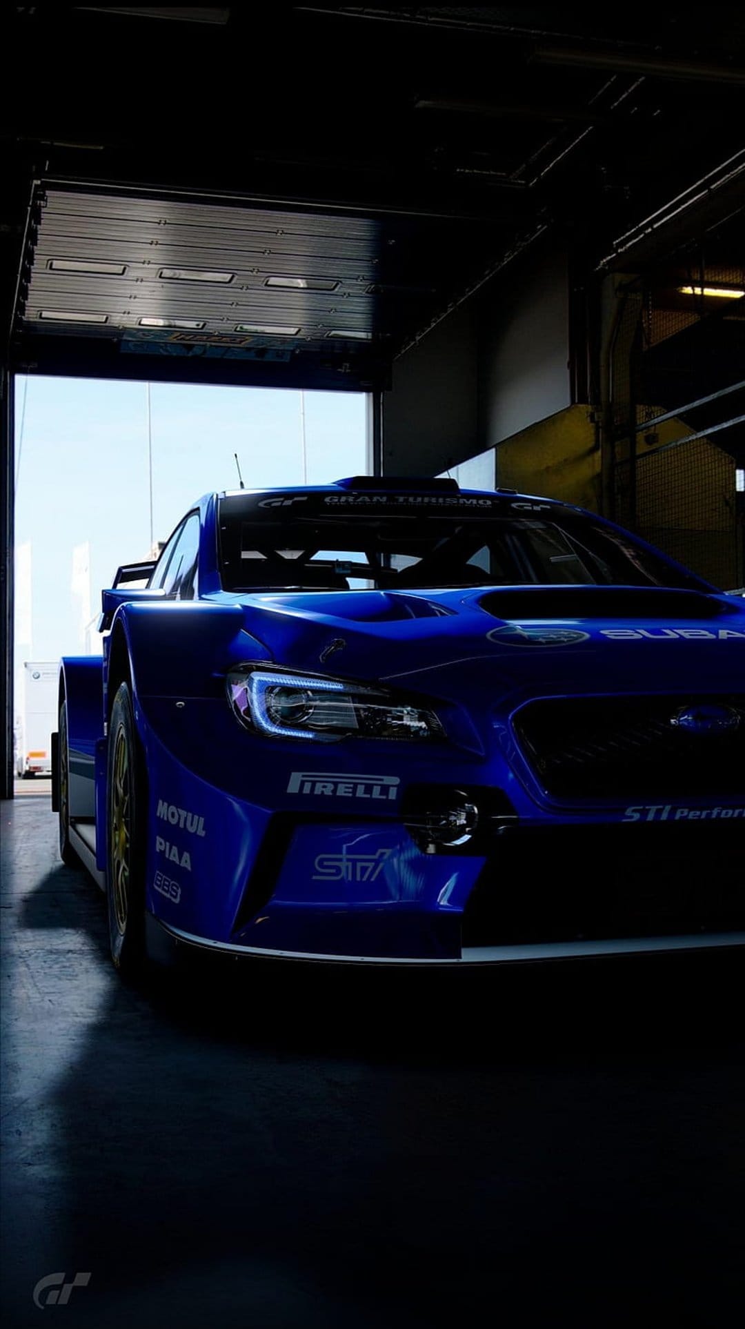 Blue Subaru STI rally car with glowing headlights inside a dark garage with a bright sky visible through the door.