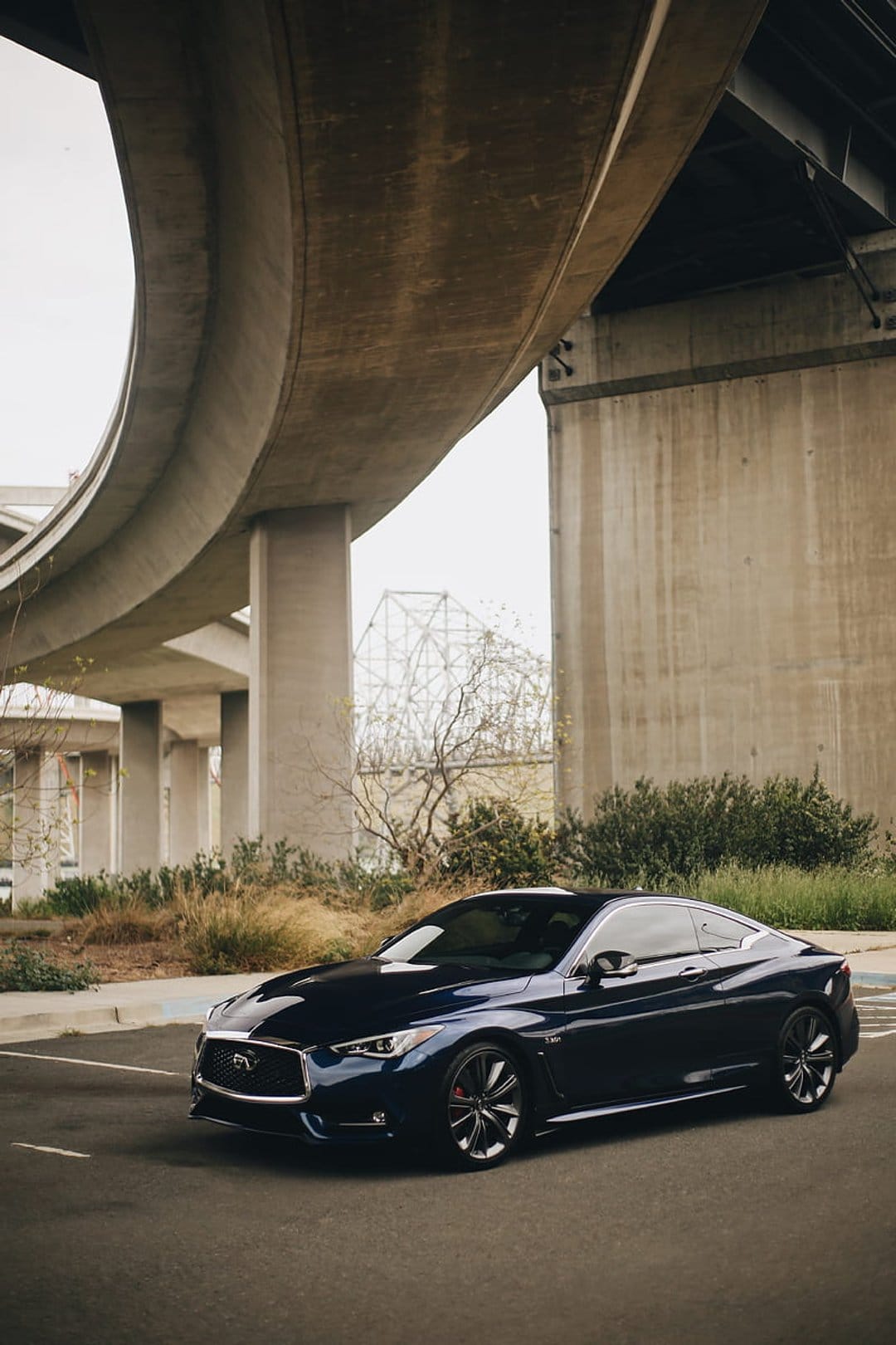 Infiniti Q60 coupe with red brake calipers parked under a curved concrete overpass on an urban asphalt road.