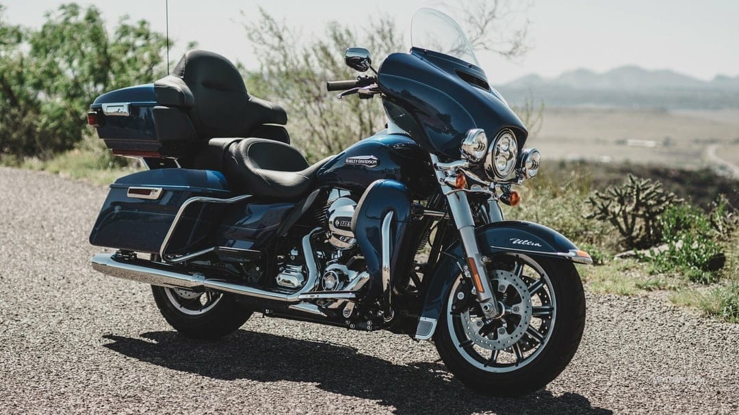 Blue Harley-Davidson touring motorcycle with chrome accents parked on a gravel path with distant mountains.