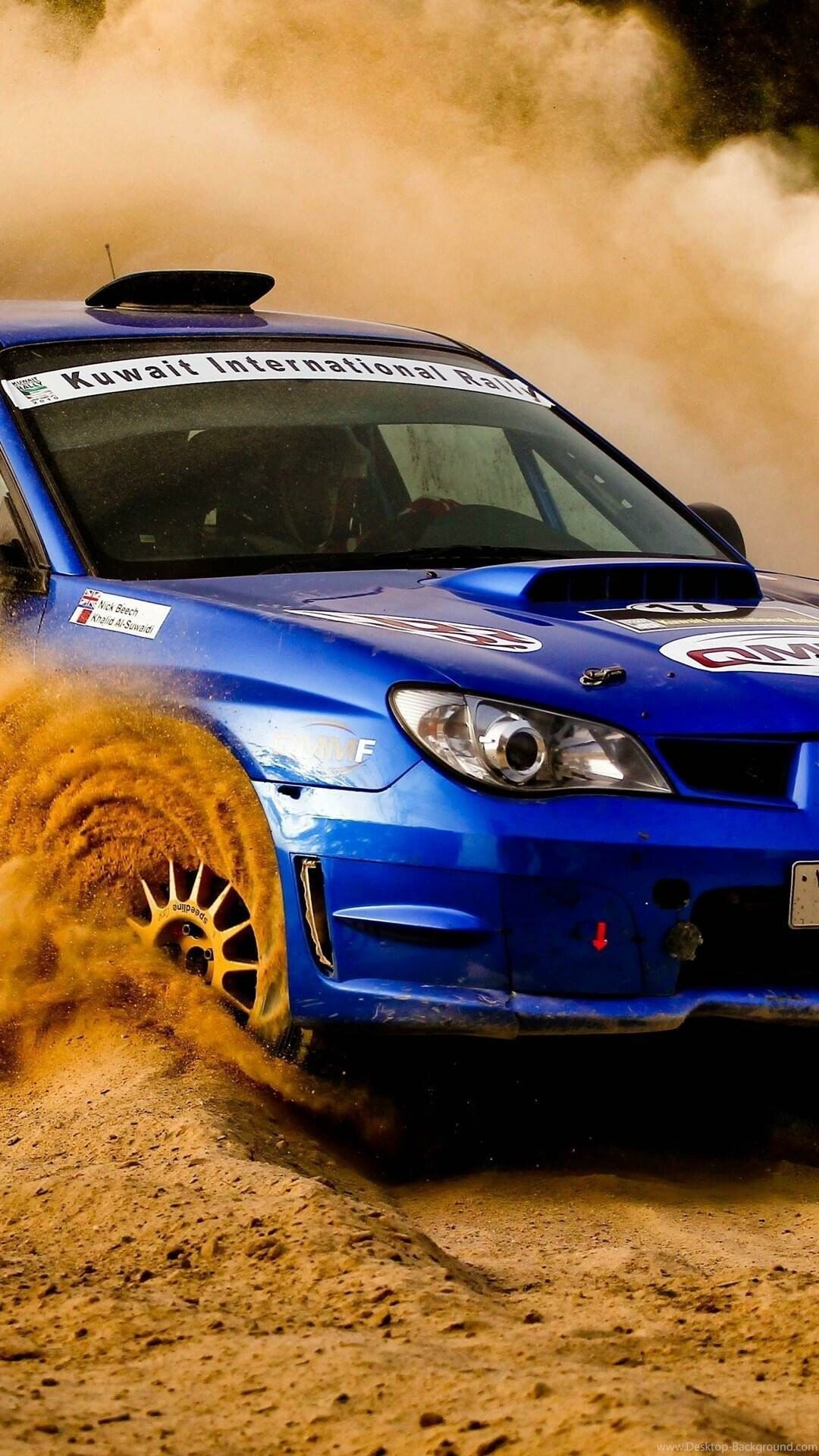 Blue rally car drifting through desert sand, creating a large golden dust spiral from its front wheel.