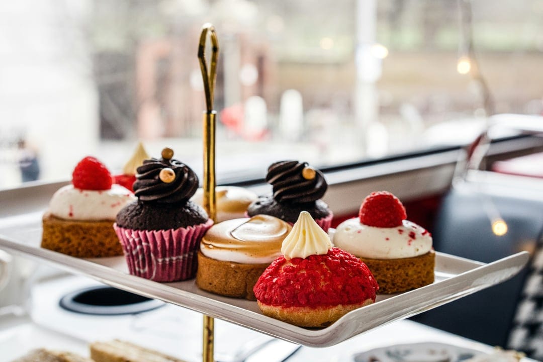 Gourmet cupcakes with chocolate frosting and berry toppings arranged on a white tiered stand with gold utensils.