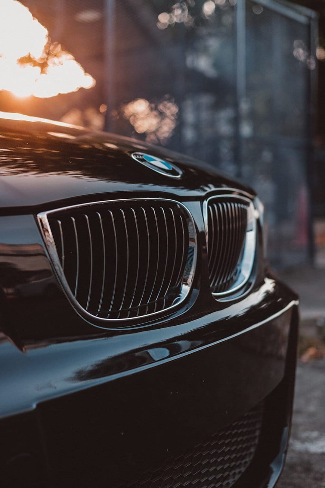Black BMW kidney grille with chrome trim reflecting a golden sunset against a blurred background.
