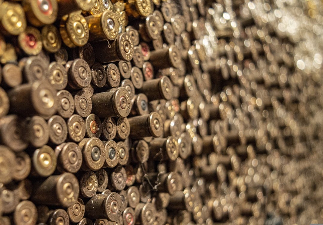 Spent brass shell casings stacked in a dense vertical pattern with shallow depth of field and metallic tones.