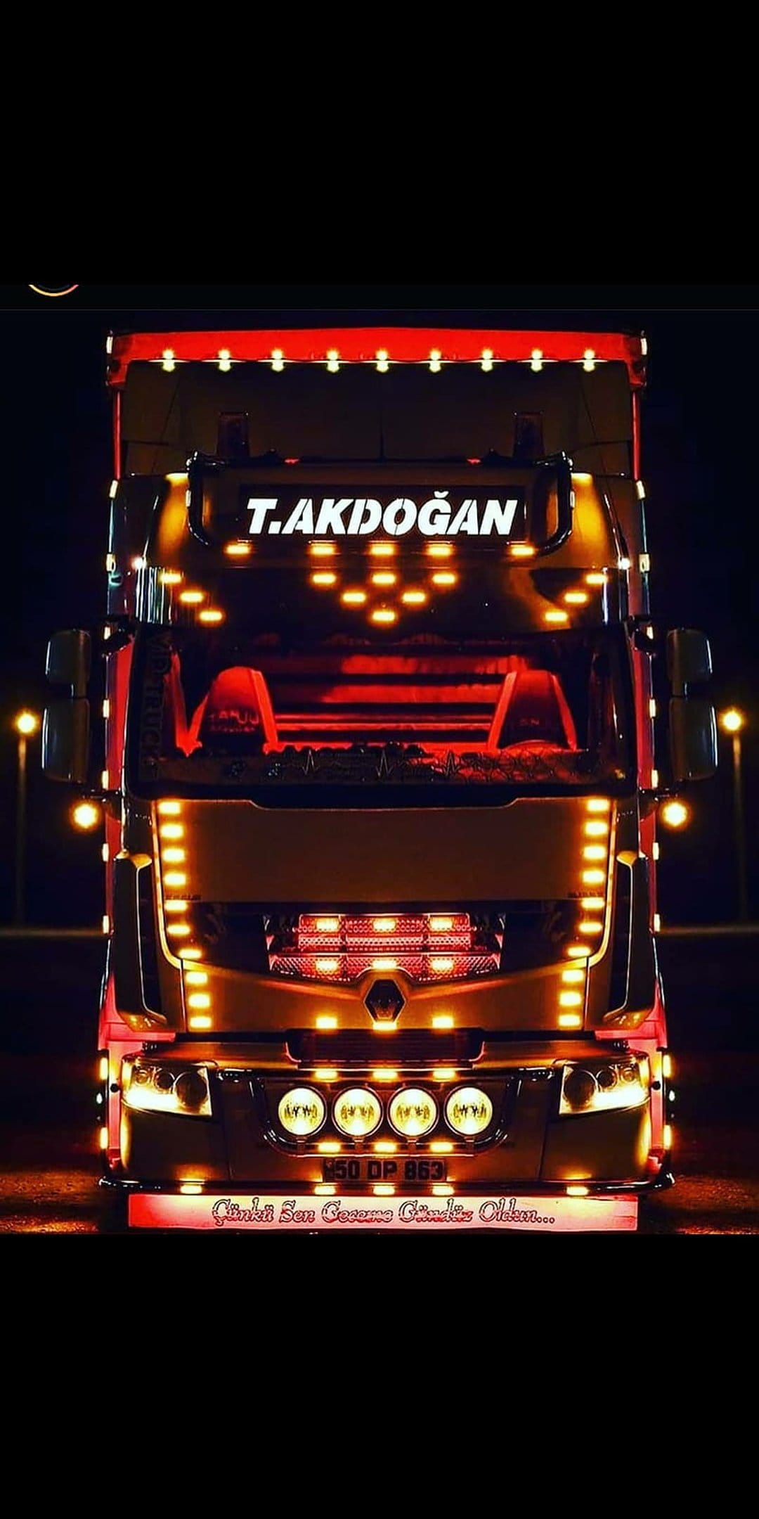 Semi-truck with a brightly lit chrome grille and decorative LED patterns glows against a dark night background.