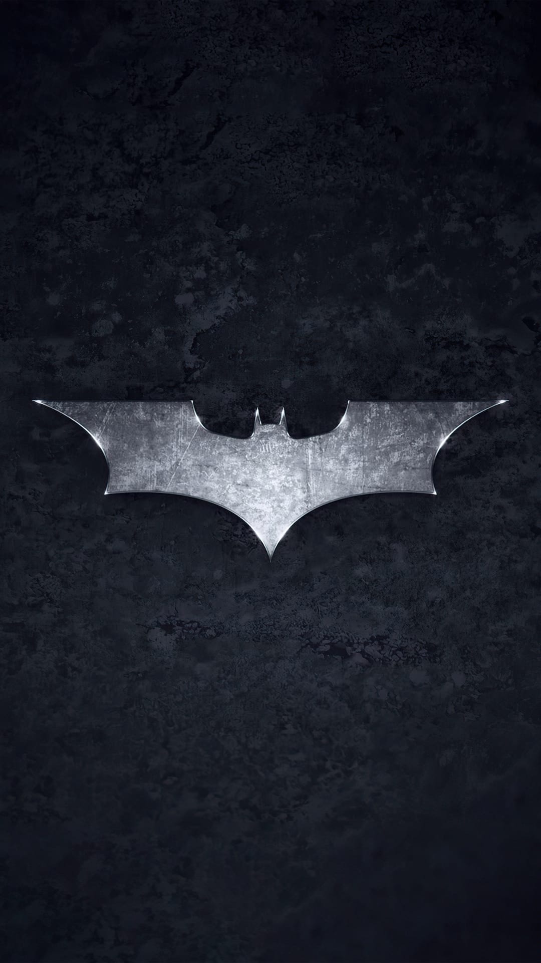 Silver Batman logo with scratches on a dark grey slate background featuring subtle edge highlights.