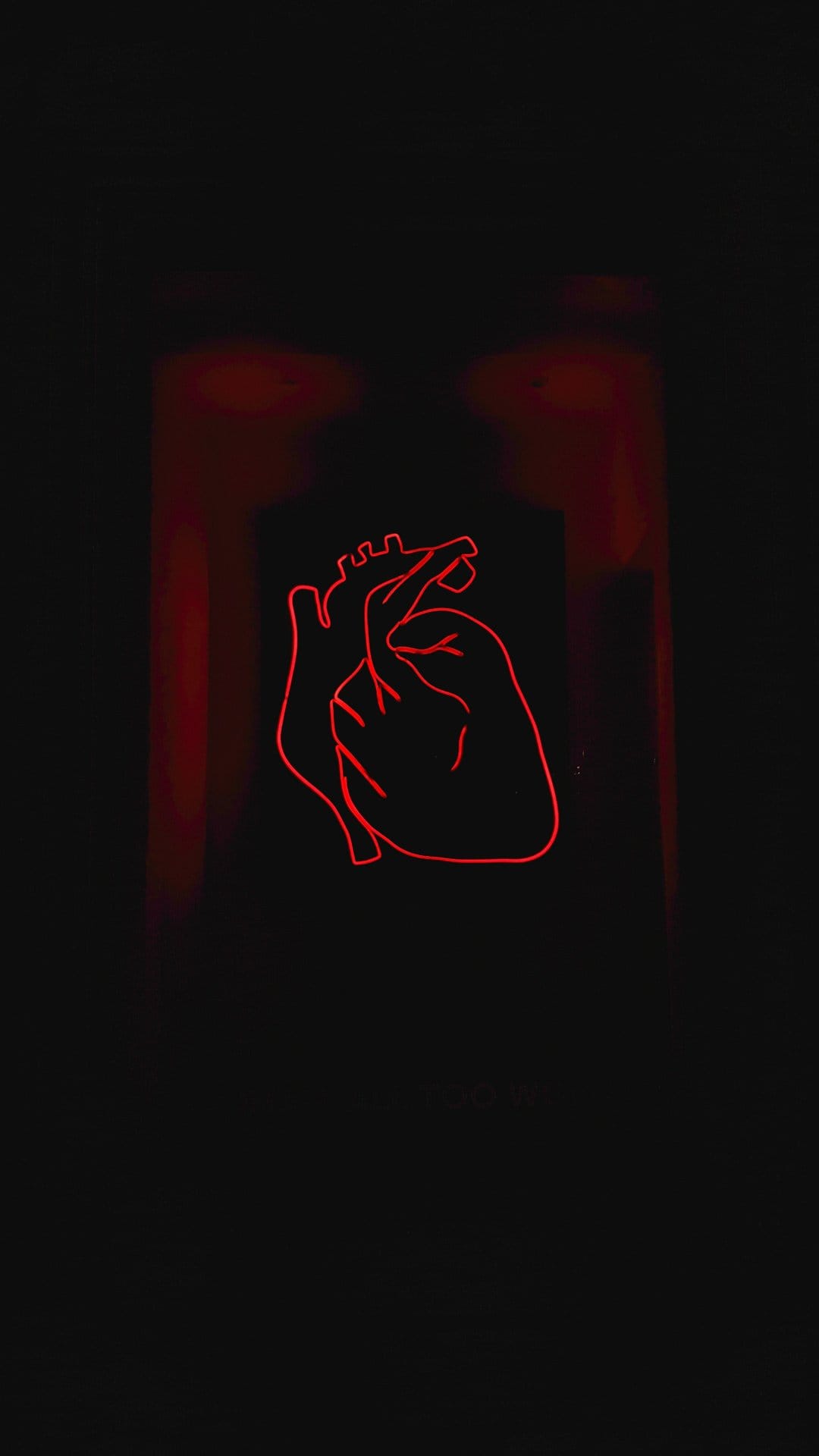 Red neon human heart outline glowing against a dark black background with soft crimson light diffusion.
