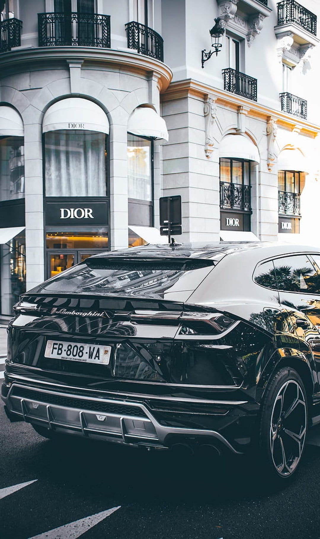 Black Lamborghini Urus SUV parked on a city street in front of a Dior boutique with arched stone windows.