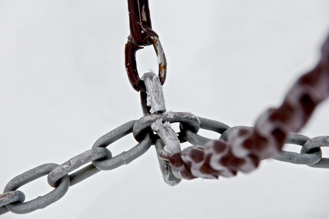 Metal chains covered in white frost and ice crystals against a bright, blurred backdrop in a macro composition.