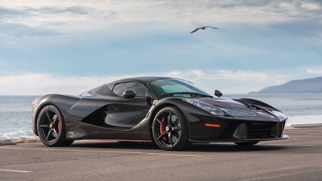 Black Ferrari LaFerrari Aperta parked on a coastal asphalt road with the ocean and a bird in the background.