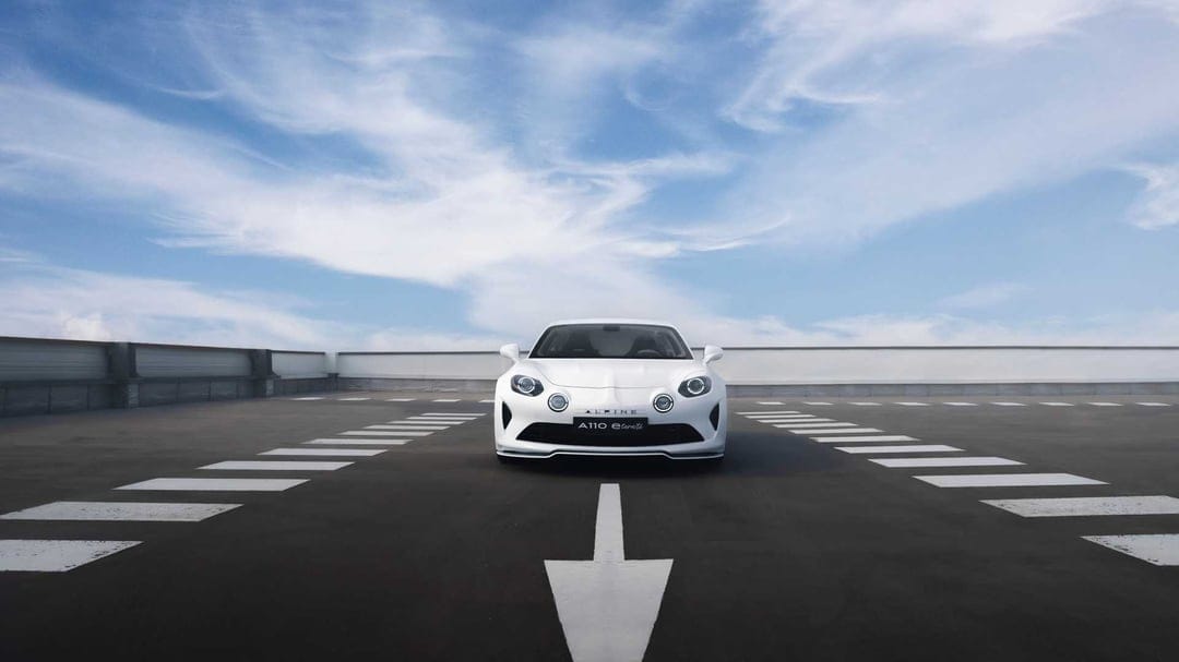 White Alpine A110 sports car centered on a rooftop parking lot under a bright blue sky with wispy clouds.
