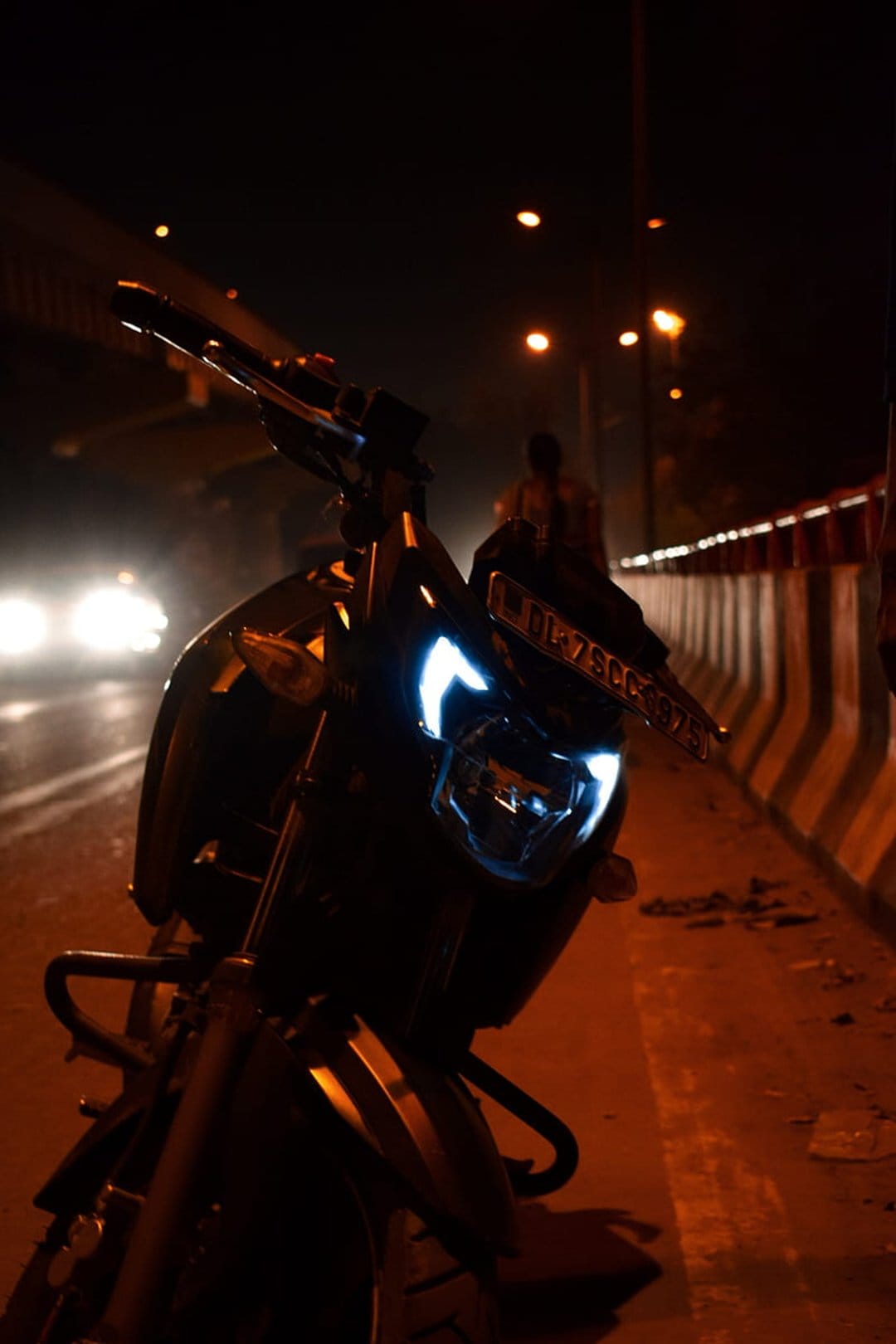 Motorcycle LED headlights illuminate a dark city street with soft bokeh lights in the urban background.