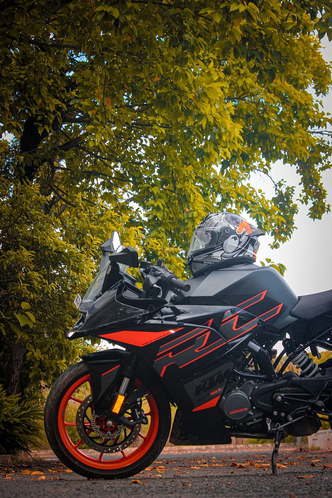 KTM RC motorcycle with orange accents parked under a leafy tree with a helmet resting on the black leather seat.