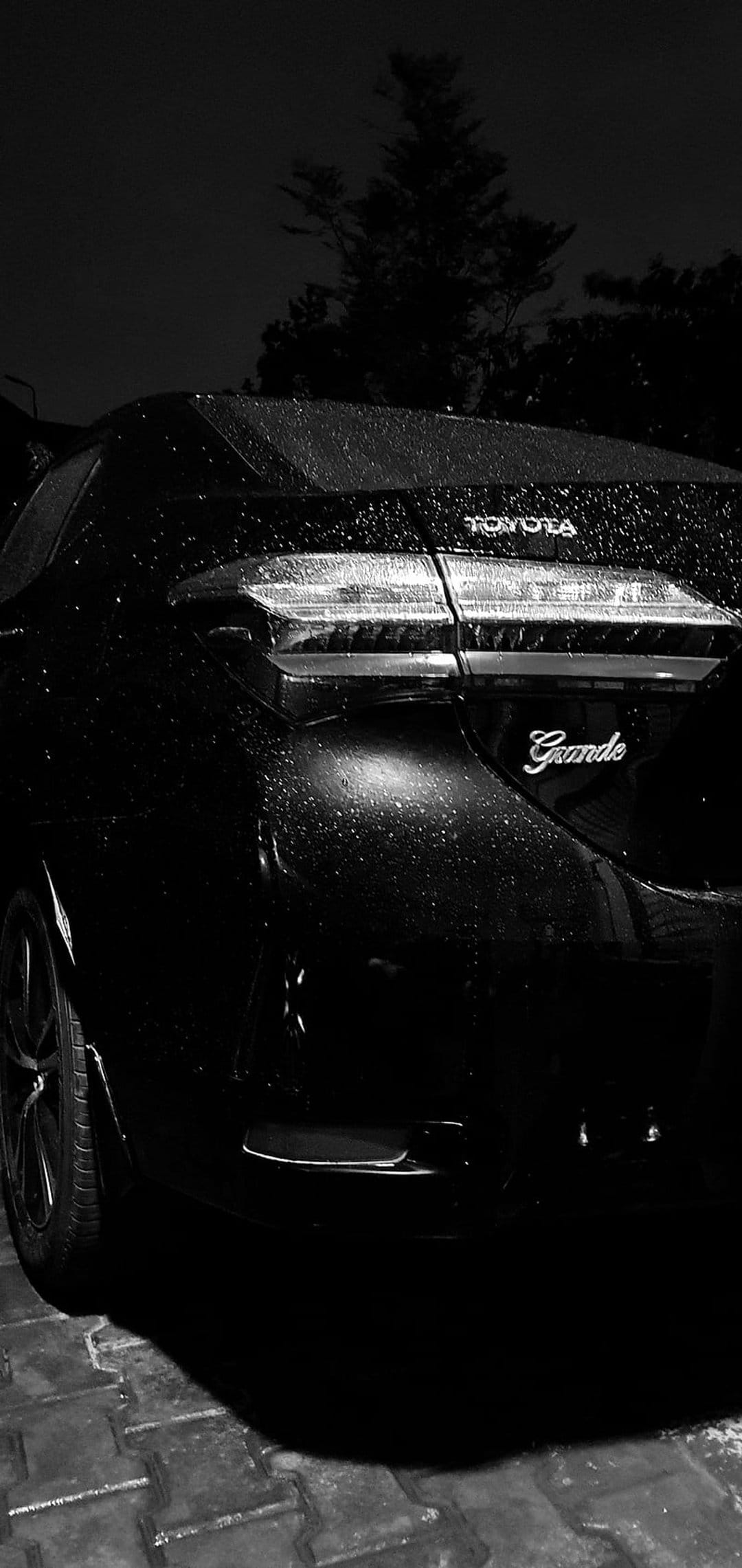 Toyota Grande sedan with water droplets on its black surface at night, illuminated by soft ambient reflections.