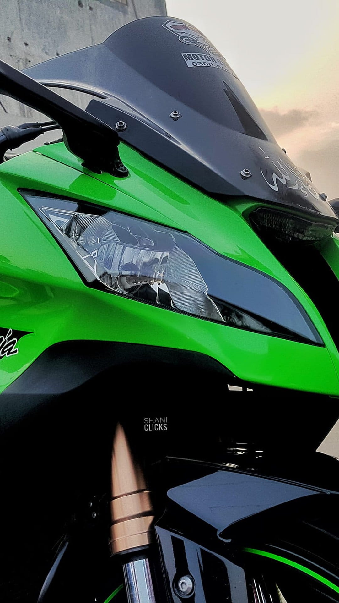 Green sportbike front fairing and glass headlight with aerodynamic lines against a blurred neutral backdrop.