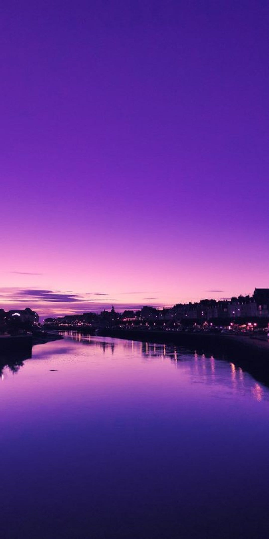 Purple twilight sky reflections shimmer across calm water while distant city lights glow along the horizon.
