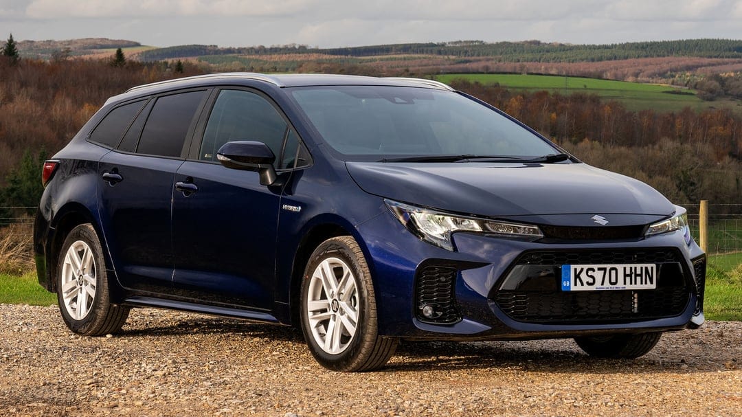 Dark blue Suzuki Swace Hybrid station wagon parked on gravel with rolling green hills and trees in the background.