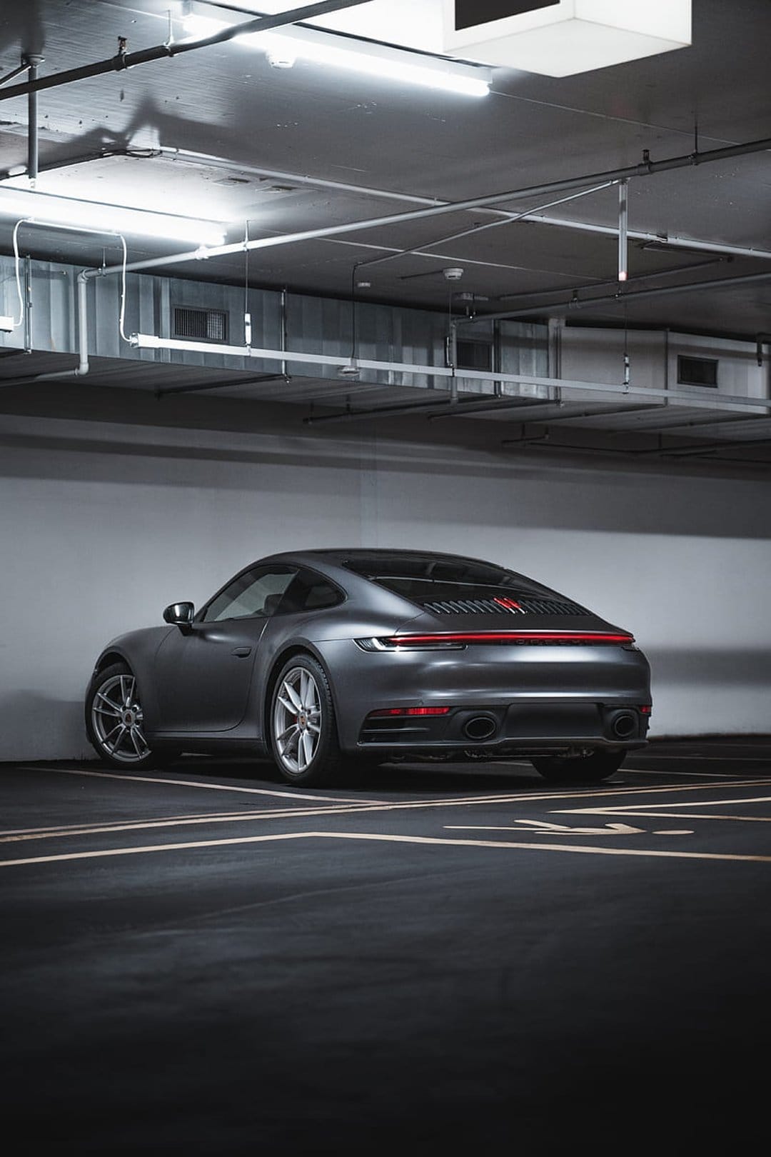 Porsche 911 rear view with glowing red lights parked on dark asphalt inside a concrete industrial garage.