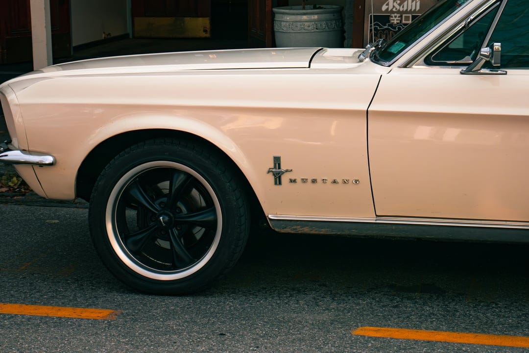 Vintage Ford Mustang fender with a chrome pony badge and black alloy wheel parked over yellow road lines.