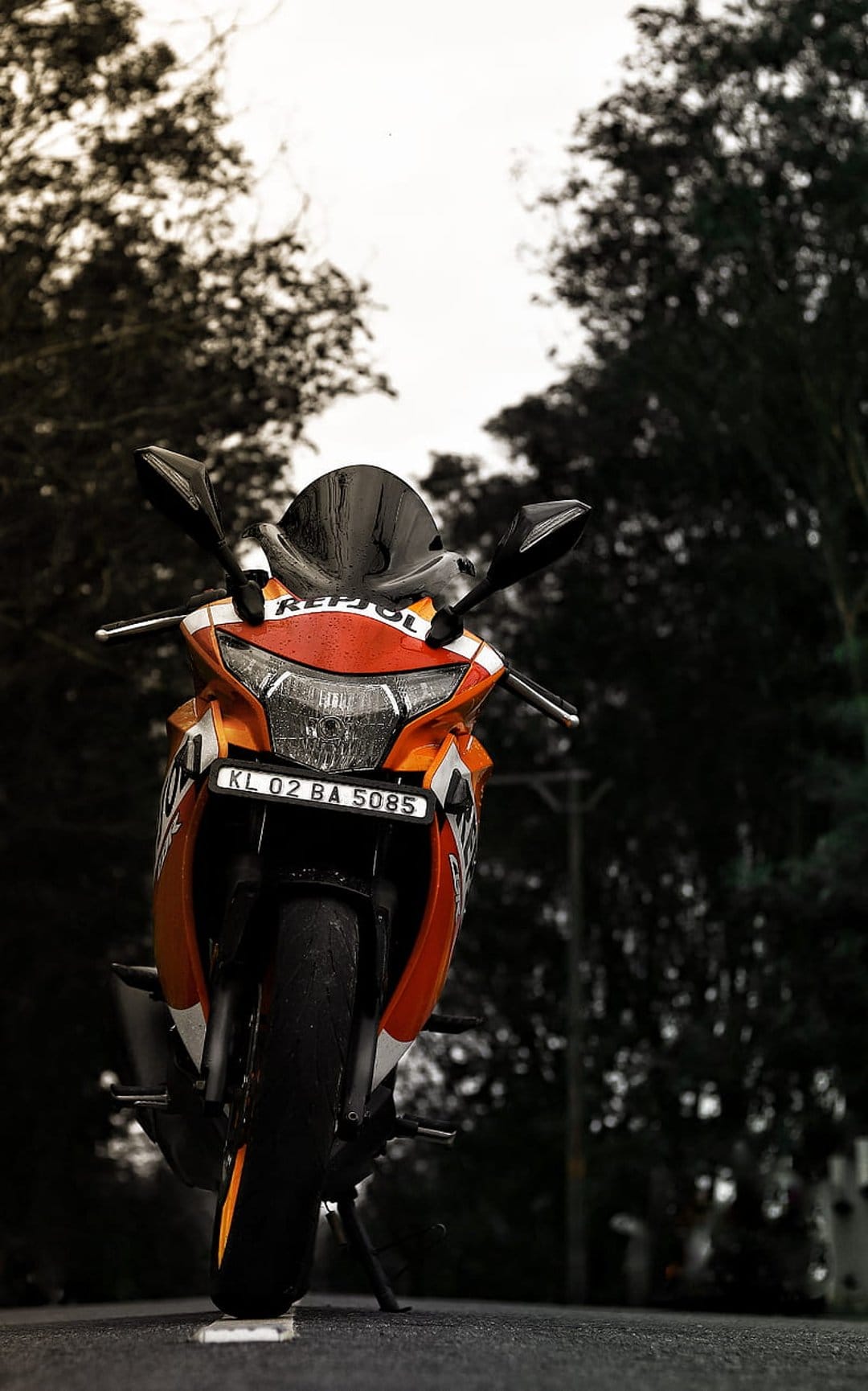 Honda CBR Repsol motorcycle in orange parked on asphalt with blurred green trees under an overcast sky.