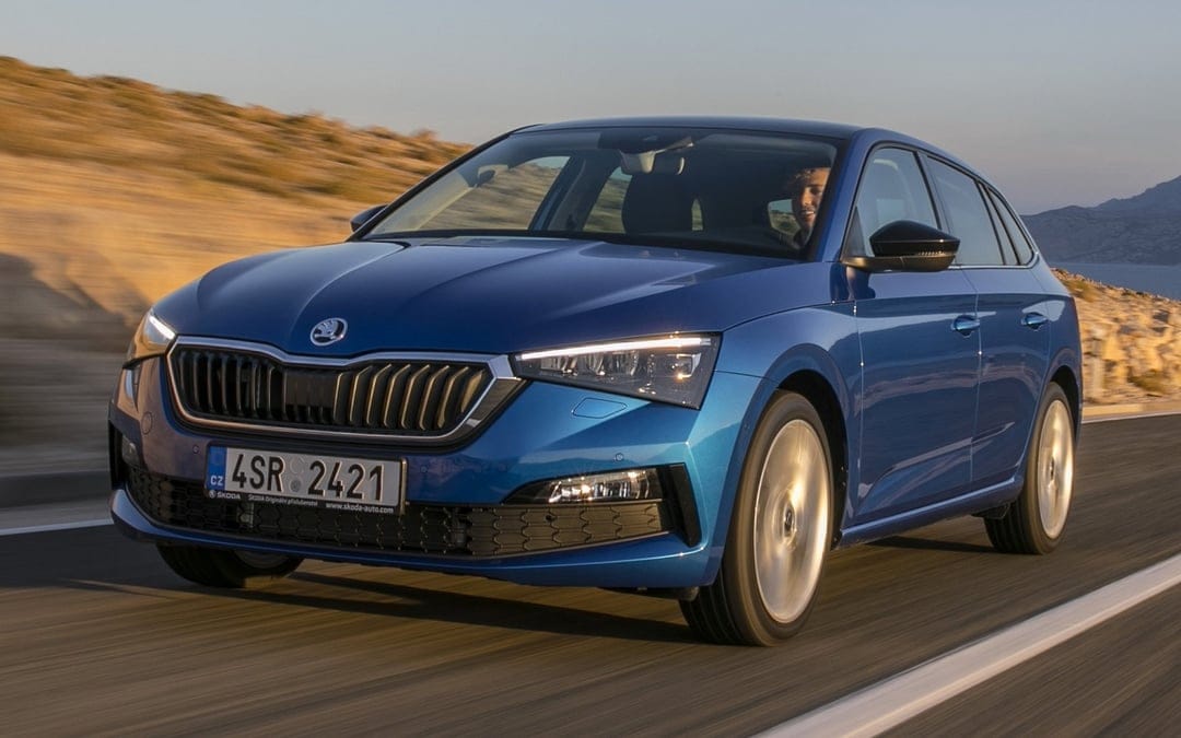 Blue Skoda Scala hatchback driving on a scenic road at sunset with motion blurred wheels and warm light.