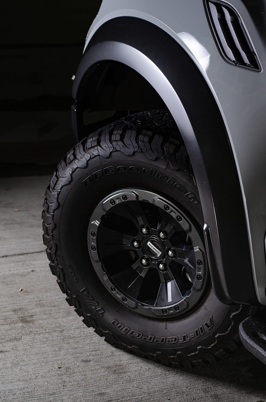 Black BFGoodrich off-road tire with deep tread patterns mounted on a glossy custom rim under a grey fender flare.