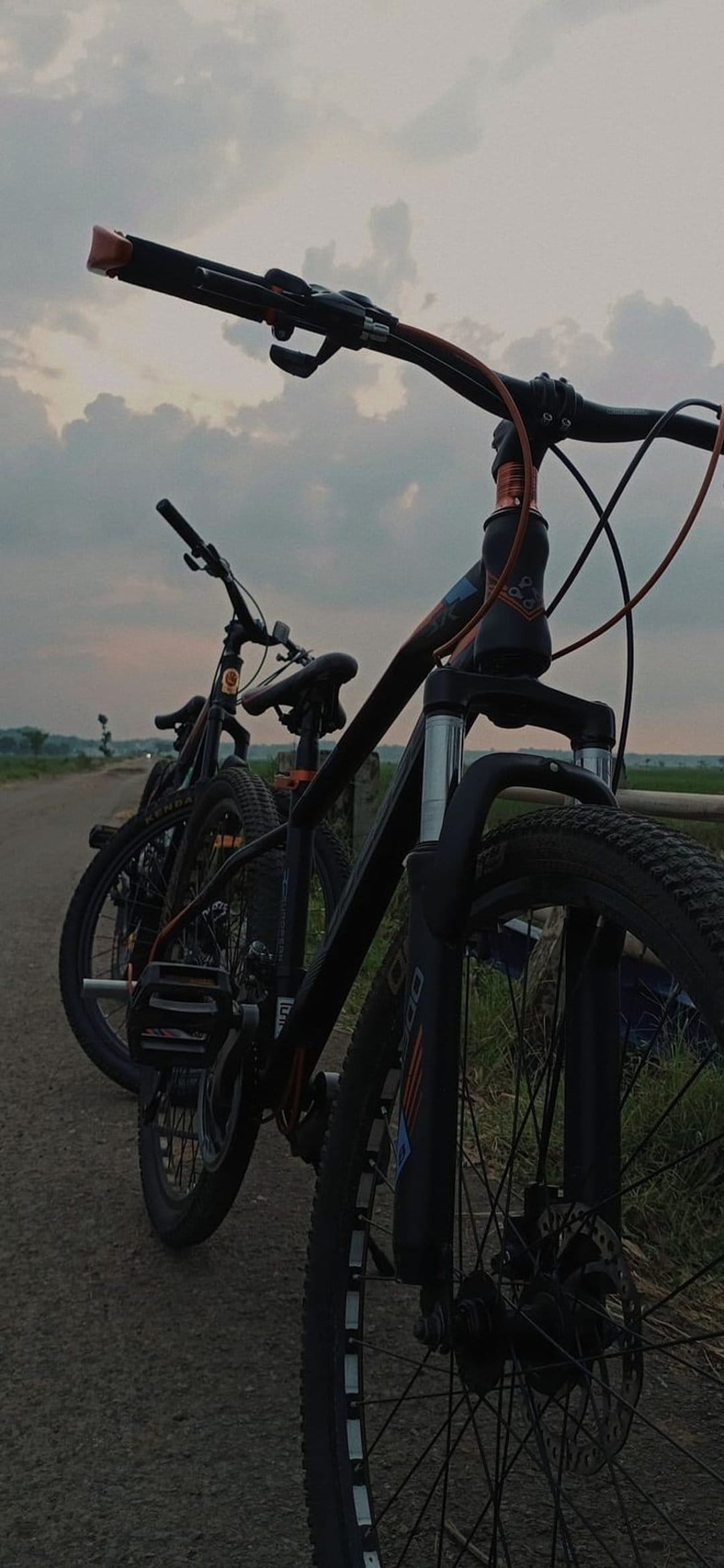Two black mountain bikes parked on a dirt road during a vibrant sunset with dramatic orange-lit clouds.