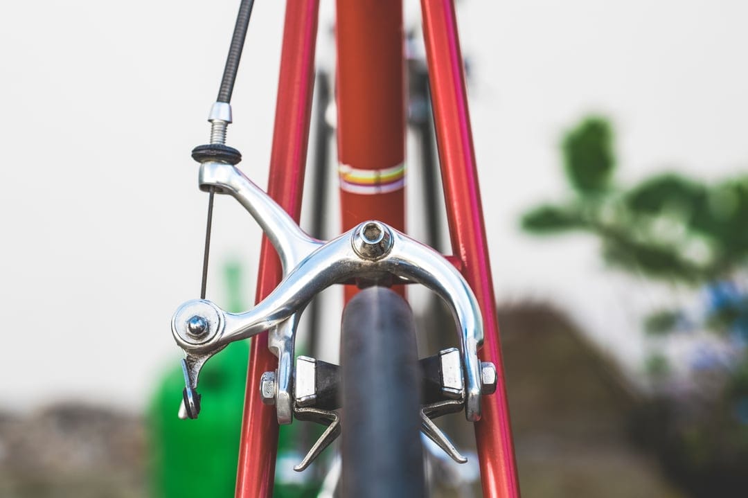Vintage red bicycle caliper brakes with polished chrome finish mounted over a black tire and pinstriped frame.