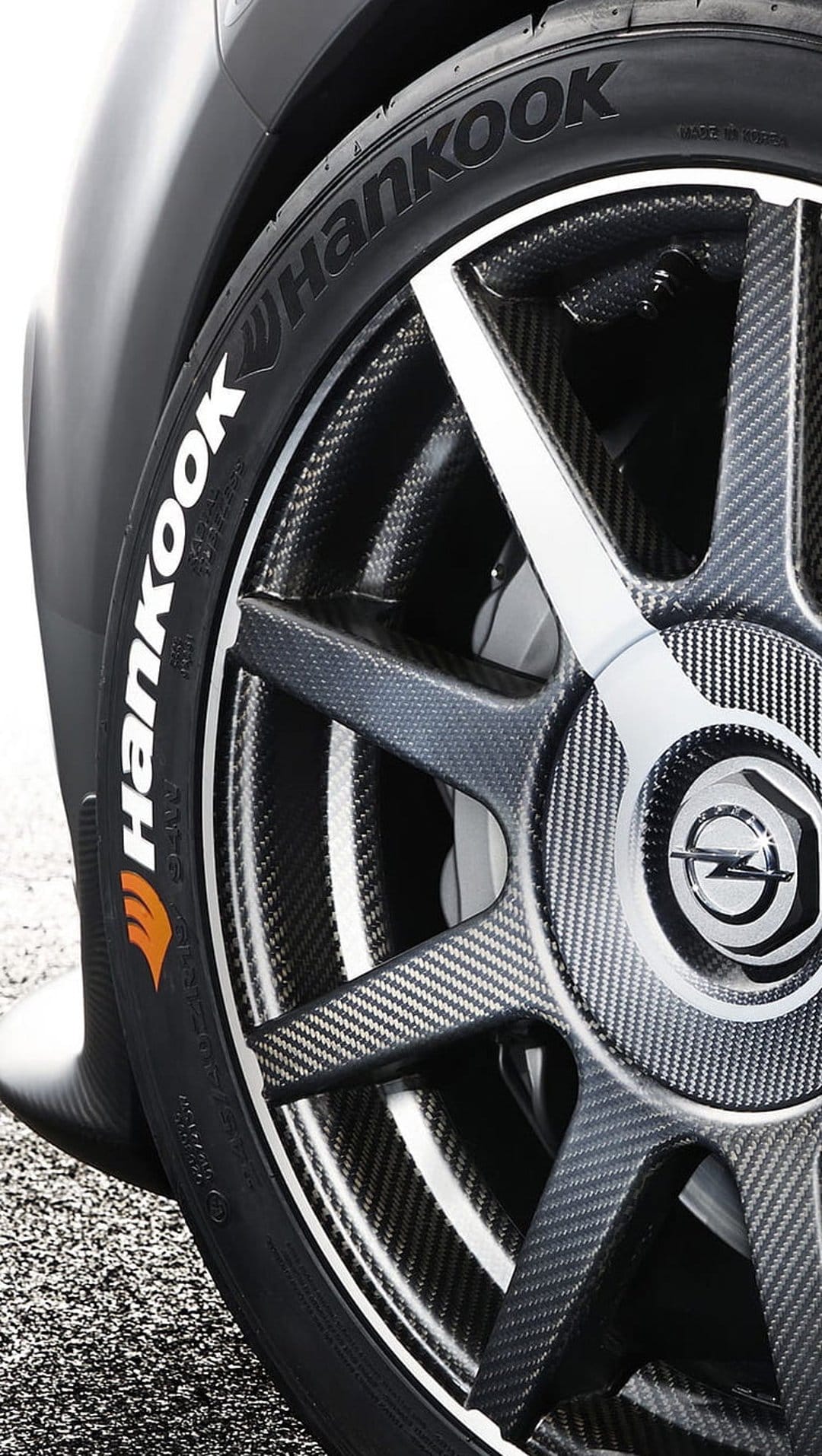 Carbon fiber Opel wheel rim with a Hankook tire featuring white sidewall lettering and intricate tread.