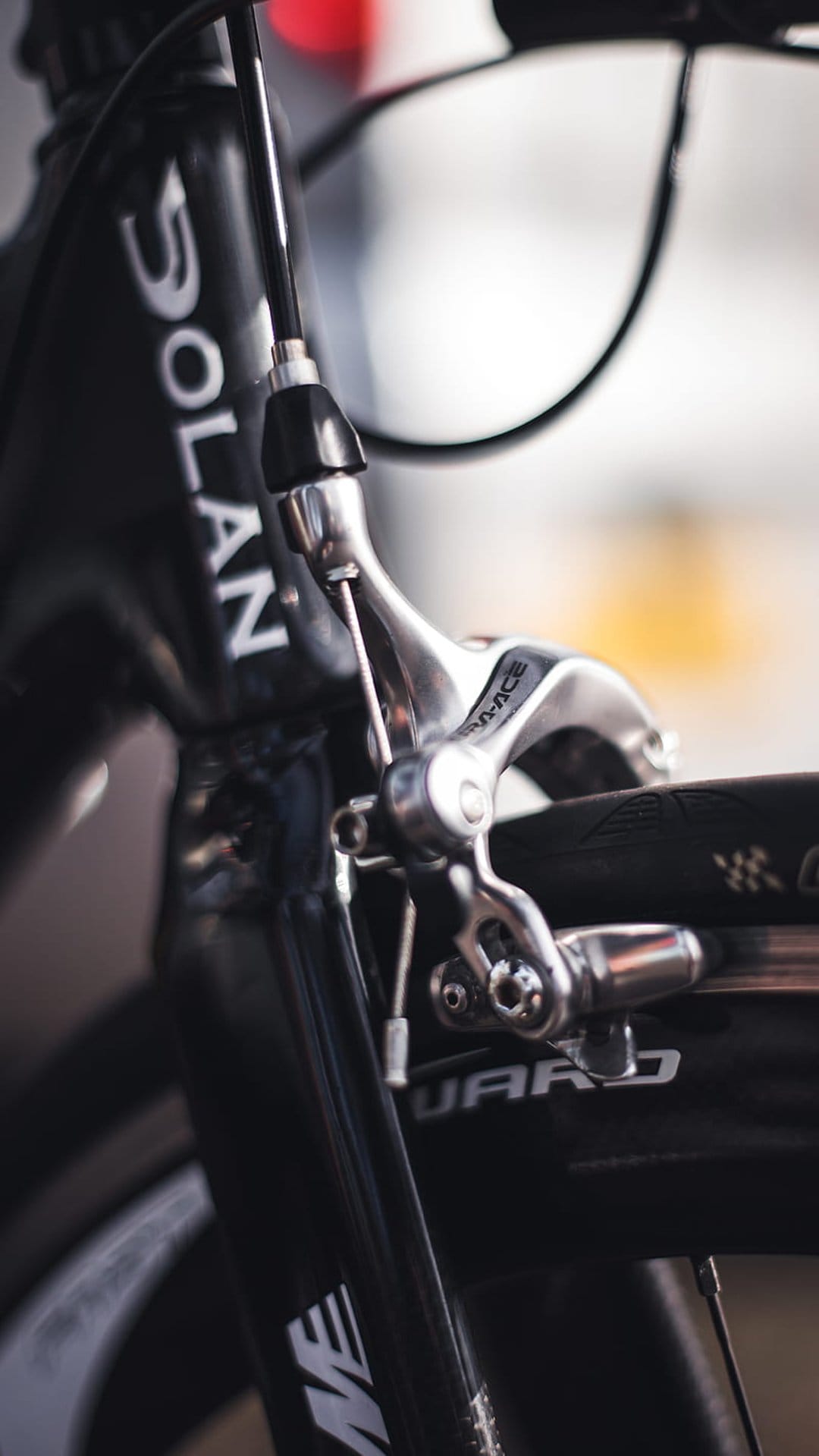 Silver front brake caliper and black bicycle frame with white lettering against a soft blurred background.