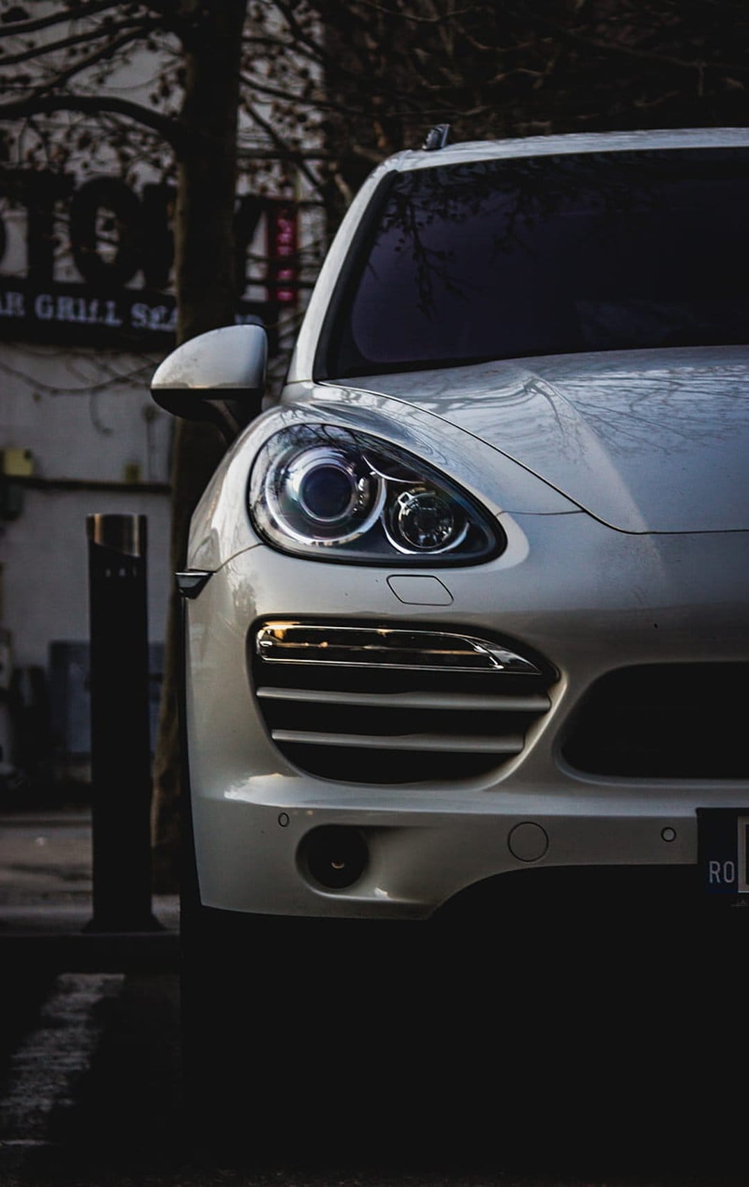 White Porsche Cayenne SUV front view showing LED headlights and chrome grille parked on a sunlit city street.