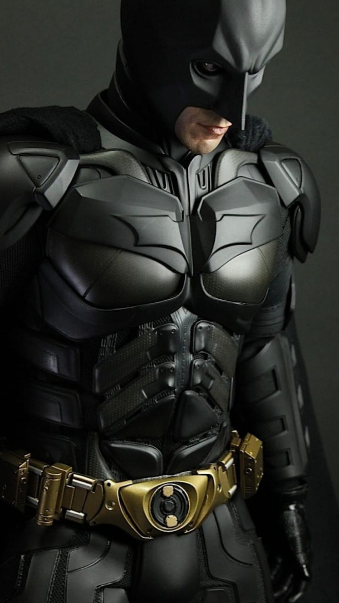 Batman in tactical armor displays a stern expression and gold utility belt in a detailed close-up shot.