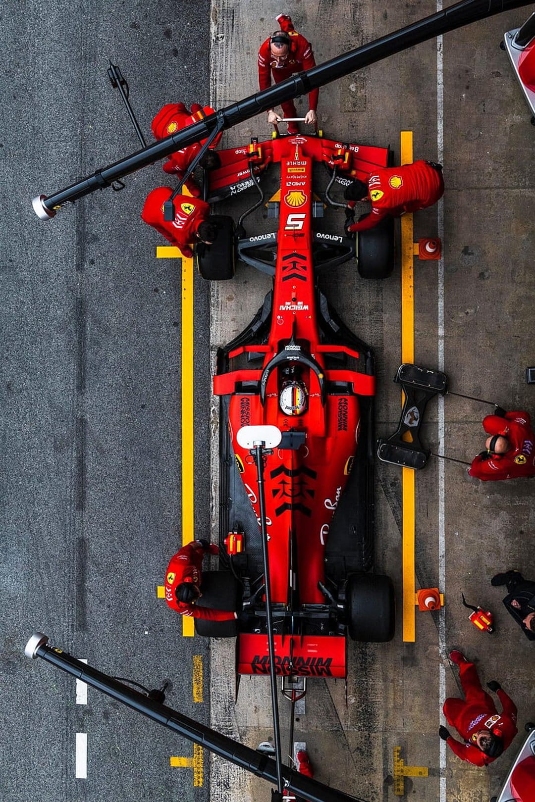 Ferrari pit crew mechanics in red uniforms service a Formula 1 car during a top-down aerial pit stop sequence.