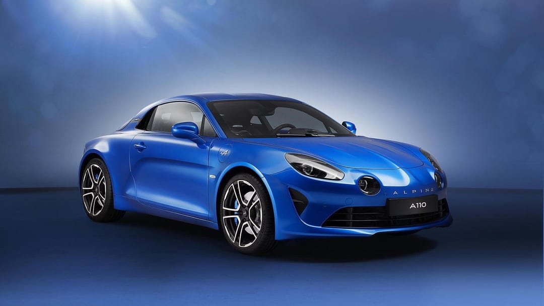 Blue Alpine A110 sports car in a studio with soft lighting, side-front view against a blue backdrop.