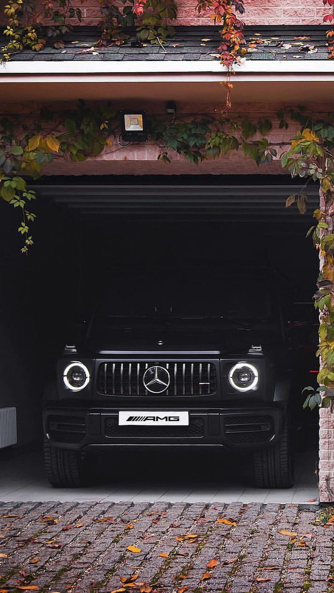 Black Mercedes-AMG G-Wagon SUV parked inside a brick garage framed by cascading red and orange autumn leaves.