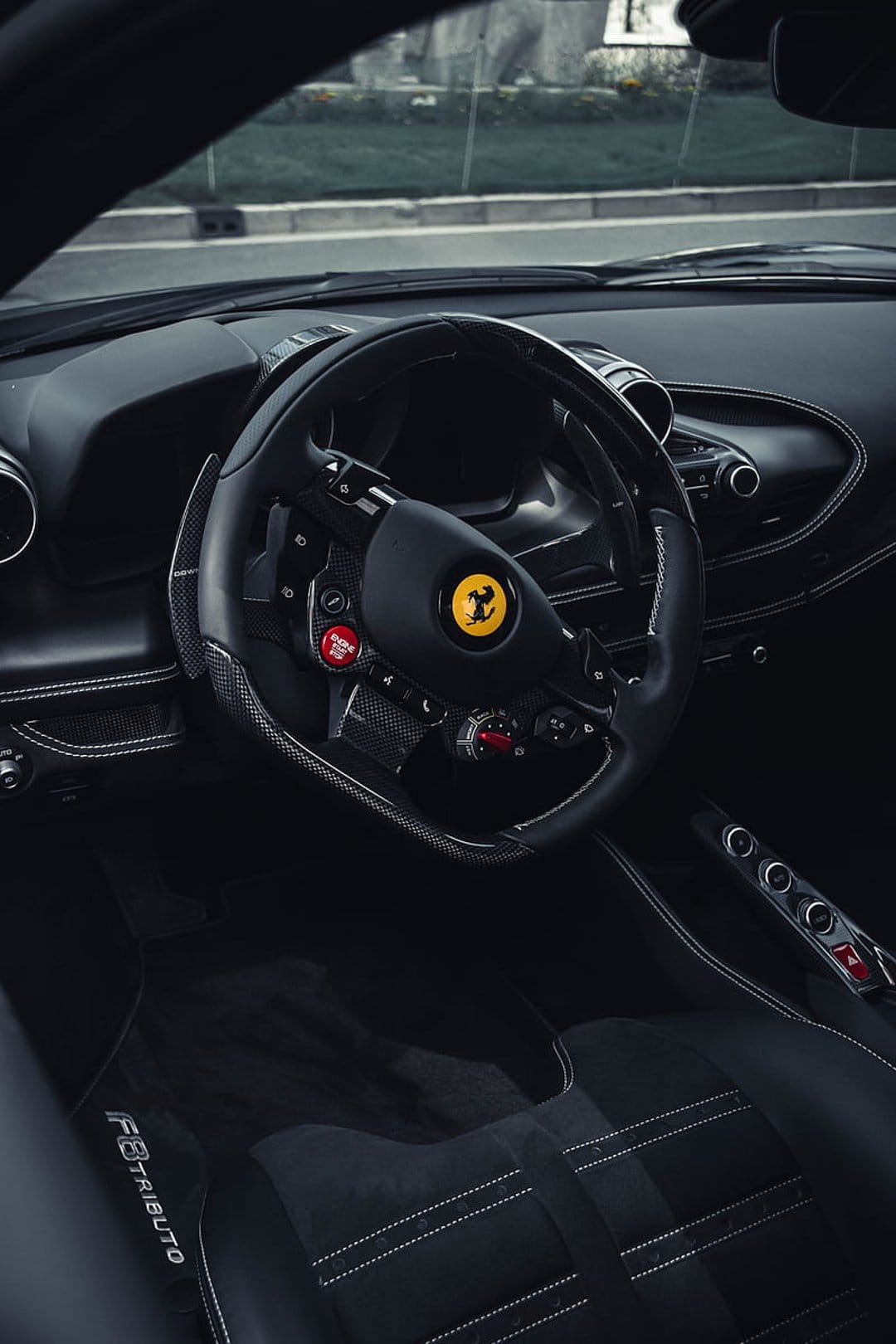Ferrari F8 Tributo steering wheel with F1 controls and red stitching inside a carbon fiber cockpit.