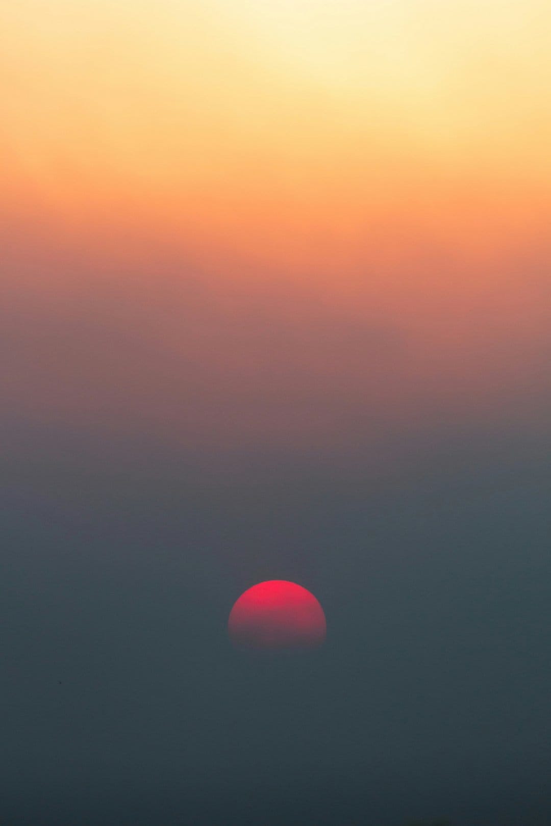 Deep red sun partially obscured by thick atmospheric haze against a glowing orange and pink dusk sky.