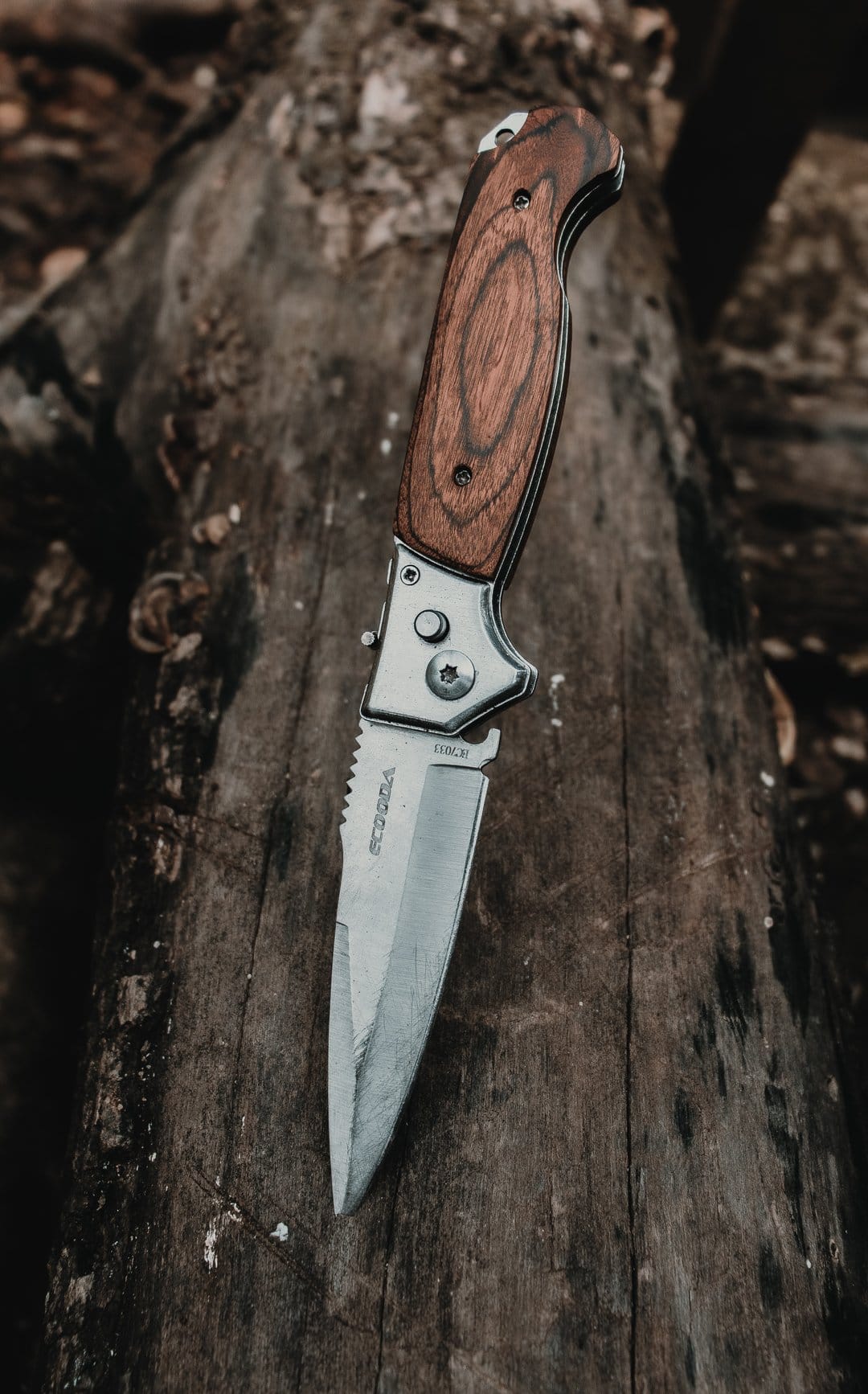 Stainless steel folding knife with a brown wood handle and serrated blade lying on dark weathered wood planks.