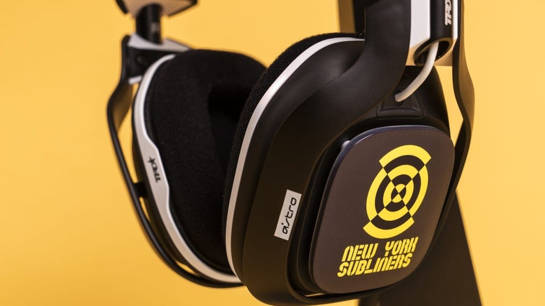 Close-up of black and white Astro gaming headphones with yellow NYSL branding against a yellow background.