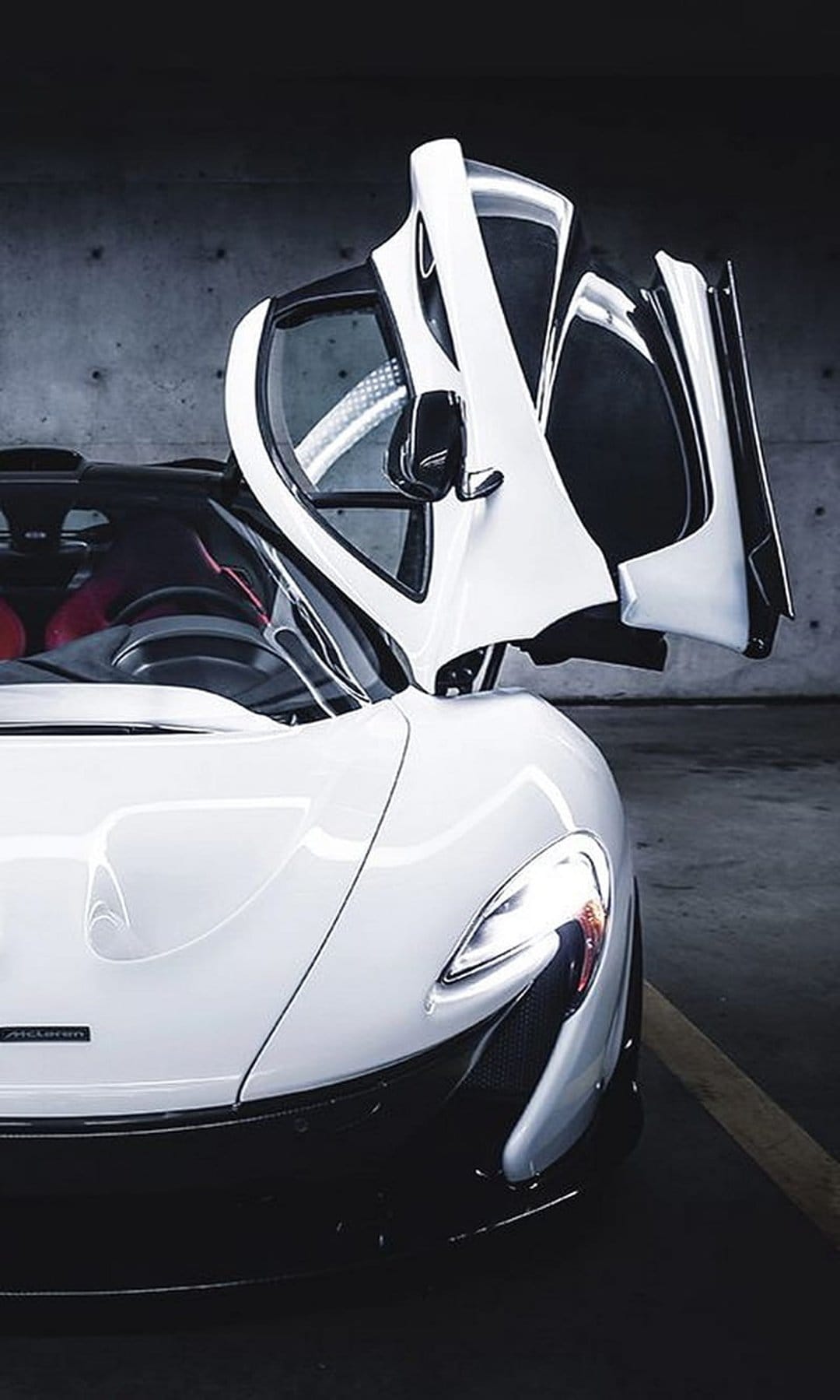 White McLaren P1 supercar with upward-opening doors revealing a red interior inside a dimly lit concrete garage.