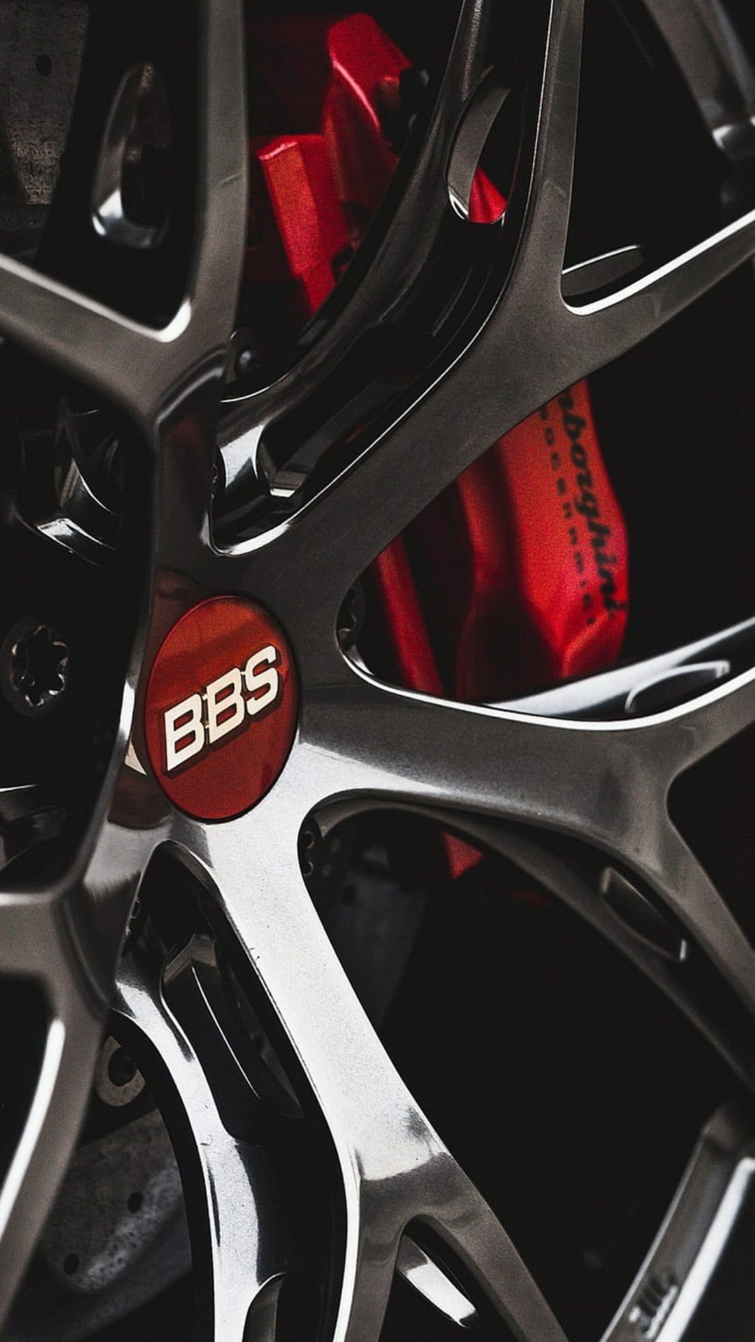 BBS alloy wheel spokes focus on a red center logo and crimson brake calipers with polished metallic surfaces.
