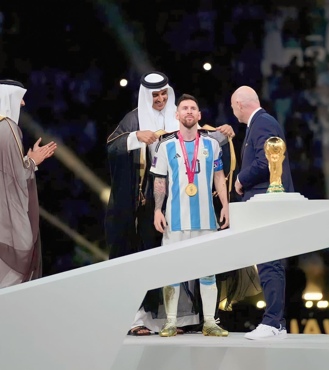 Lionel Messi clutches the golden trophy while wearing a championship medal and striped football jersey.