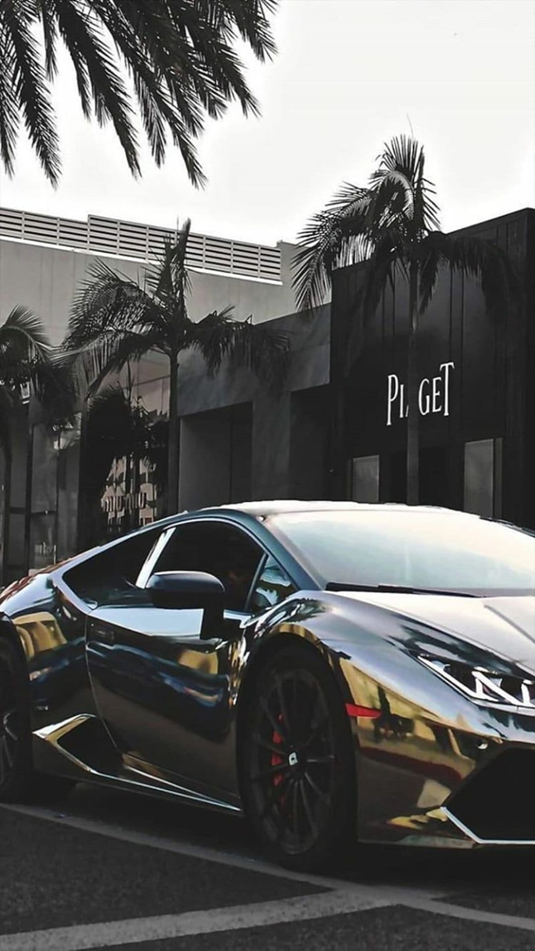 Chrome Lamborghini parked before a Piaget boutique with palm trees reflecting off the polished silver car body.