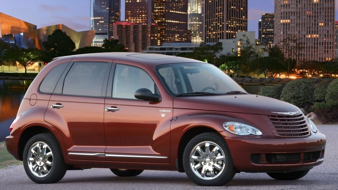 Bronze Chrysler PT Cruiser parked on a coastal road with the lit-up Los Angeles skyline at dusk in the background.