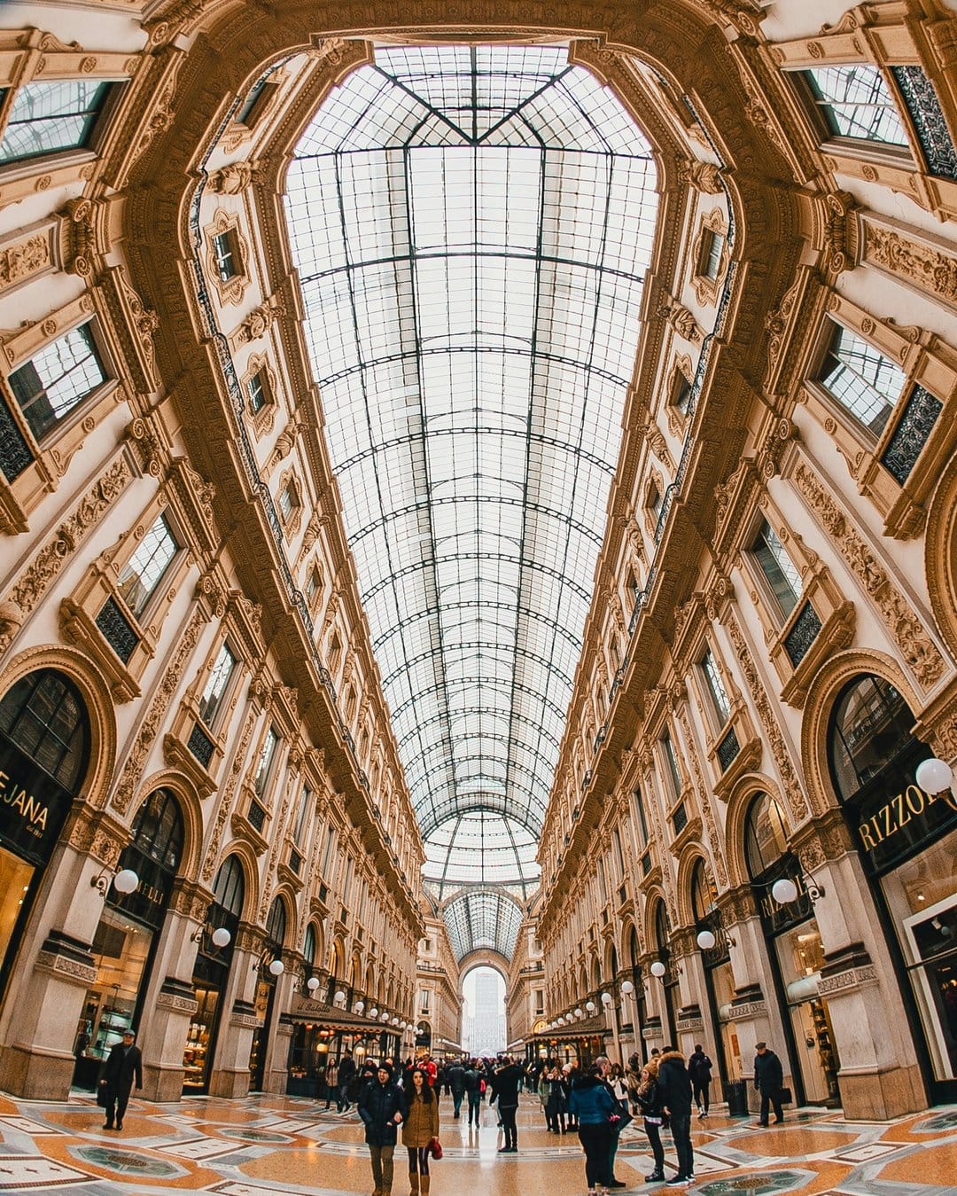 Ornate glass dome of Galleria Vittorio Emanuele II captured with a wide fisheye lens showing Italian architecture.