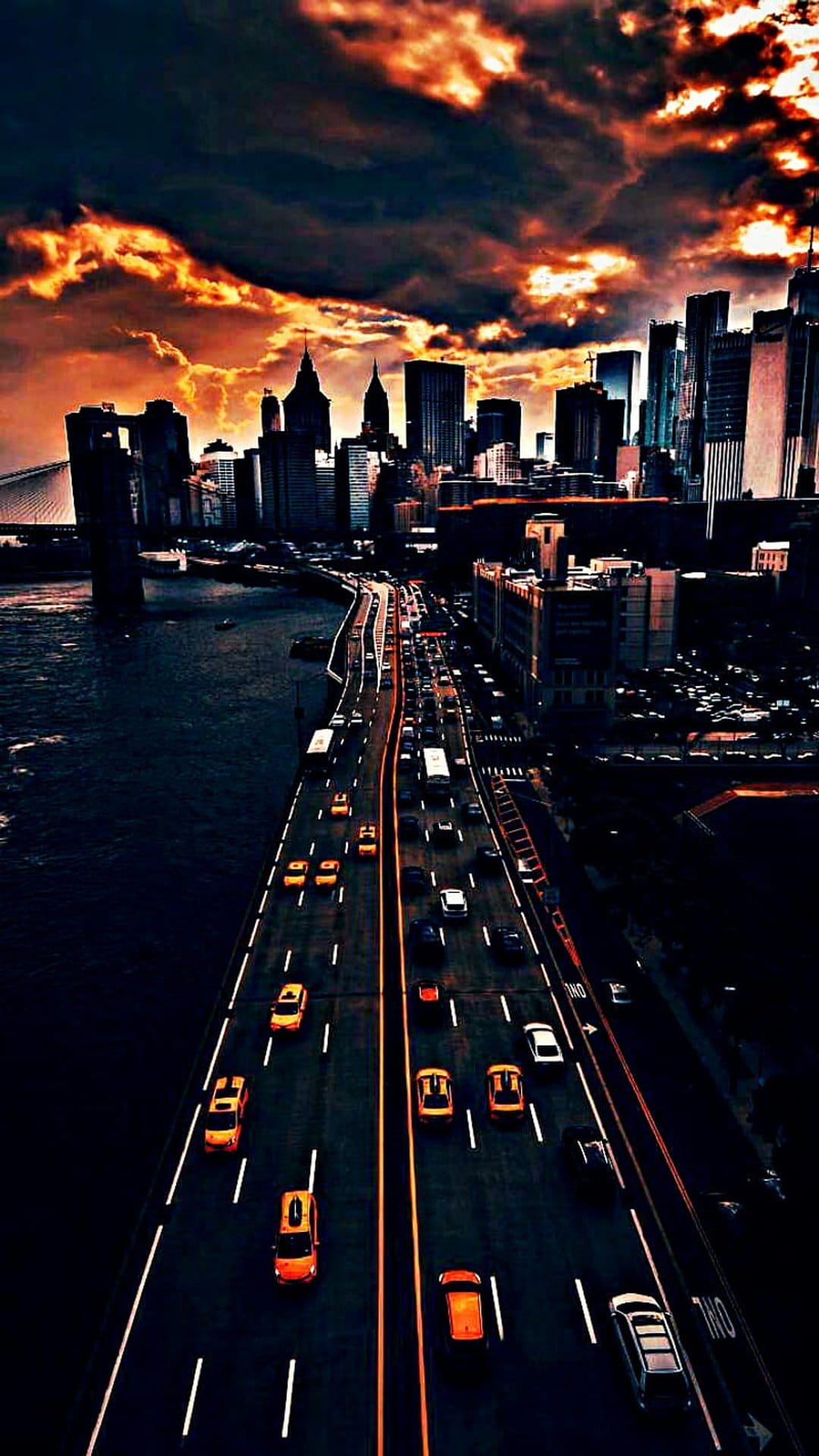 Yellow taxis and cars flow along a New York highway beneath a fiery red sunset and towering skyscrapers.