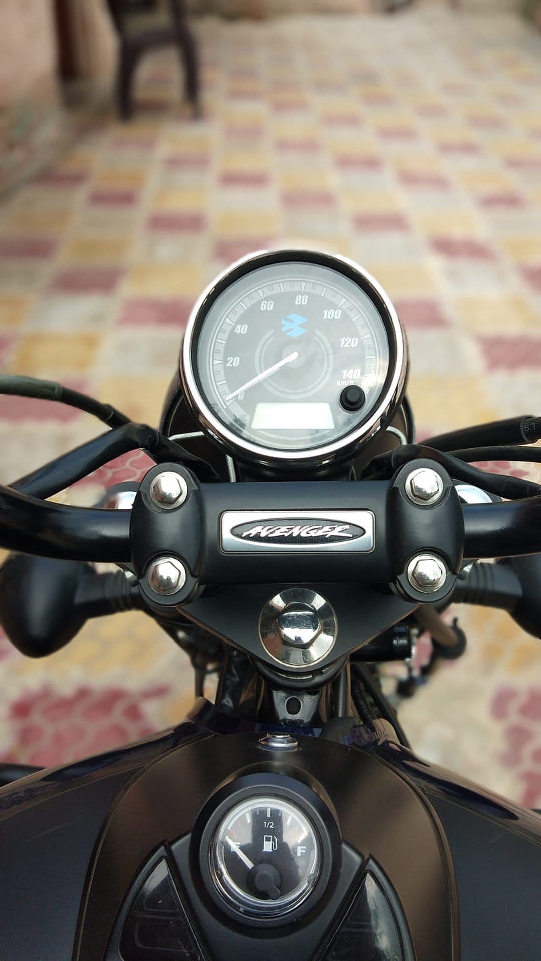 Motorcycle handlebars and instrument cluster with chrome gauges and a fuel meter under soft ambient lighting.