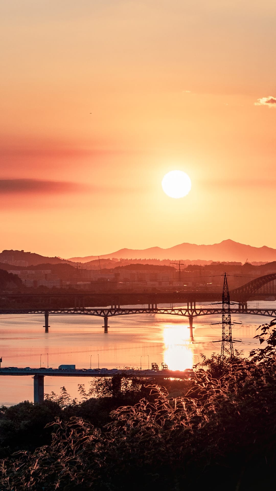 Orange sun reflects on the Han River with city bridges and hills, captured as a vertical phone background.