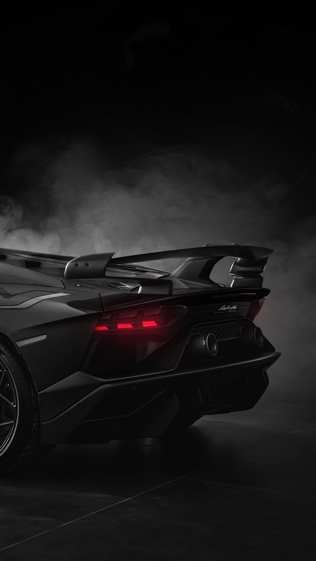 Black Lamborghini rear view features glowing red Y-shaped taillights and thick smoke on a dark road.