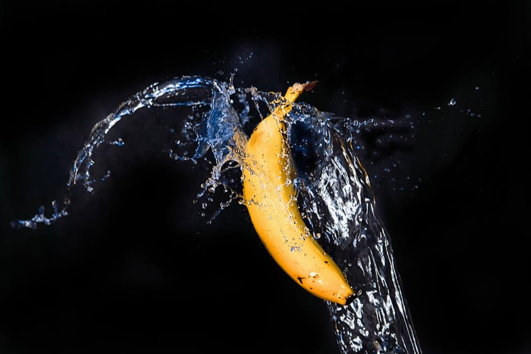Yellow banana colliding with an explosive water splash against a solid black background in high-speed detail.
